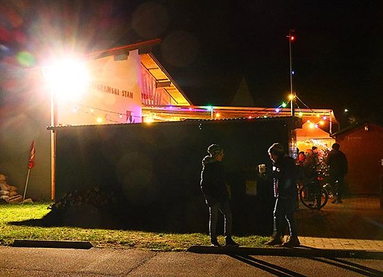 Zwei Personen stehen bei Nacht vor einem Gebäude. Das Gebäude ist beleuchtet und hat bunte Lichter. Eine Flagge ist an der Seite.