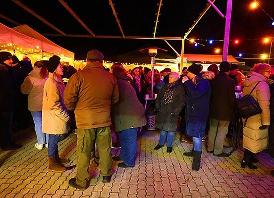 Eine Menschenmenge in Winterkleidung steht nachts bei einer Outdoor-Veranstaltung in einer Schlange. Zelte und bunte Lichter sind im Hintergrund zu sehen.