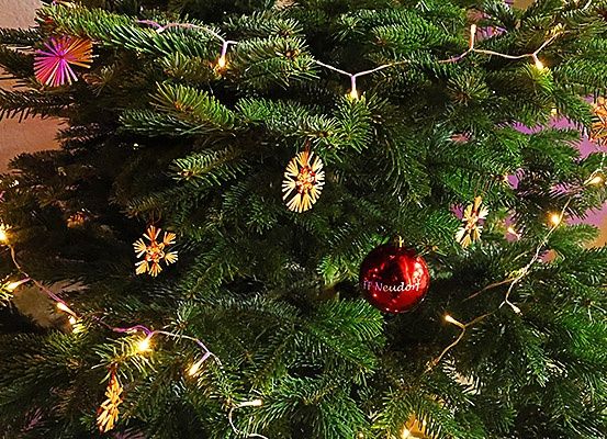 Ein Weihnachtsbaum mit einem roten Ball, Schneeflocken und bunten Lichtern geschmückt. Der Baum ist von verschiedenen Ornamenten umgeben.