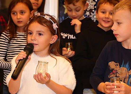Eine Gruppe von Kindern, eines mit einem Mikrofon, ein anderes mit einer Kerze, steht in einem Raum, möglicherweise während einer Zeremonie.