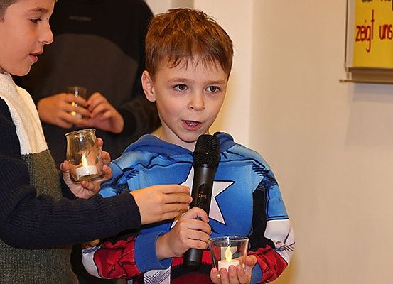 Zwei Jungen halten Kerzen, einer mit einem Mikrofon, und ein Mann im Hintergrund, der ein Glas hält.