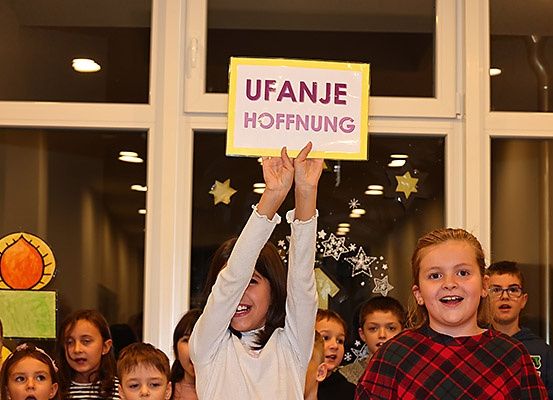 Ein Madchen halt ein Schild mit den Worten 'Ufanje Hoffnung', wahrend ein Kinderchor im Hintergrund singt.