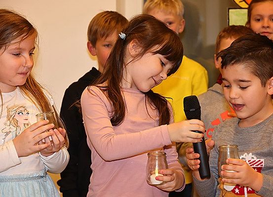 Eine Gruppe von Kindern mit Kerzen steht in einem Raum, wobei ein Mädchen ein Mikrofon hält.