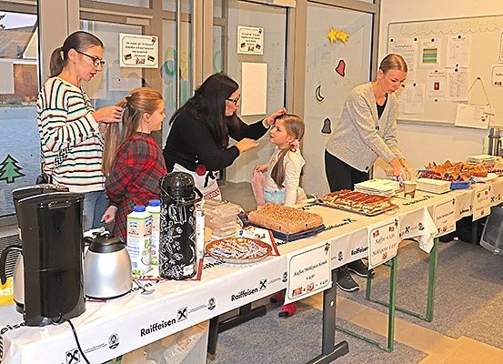 Mehrere Frauen bereiten Speisen und Getränke an einem Buffettisch in einem Klassenzimmer mit Tafel und Anschlagtafel vor.