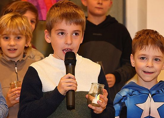 Ein junger Junge hält ein Mikrofon und eine Kerze und spricht bei einer Veranstaltung mit anderen Kindern.