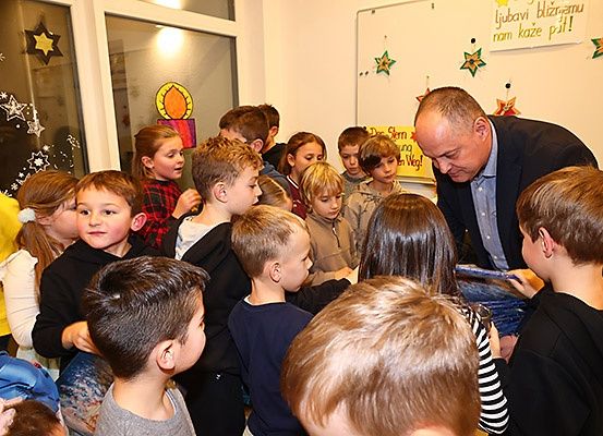 Eine Gruppe von Kindern und einem Mann im Anzug versammelt sich in einem Raum mit dekorativen Sternen und Text an der Wand.