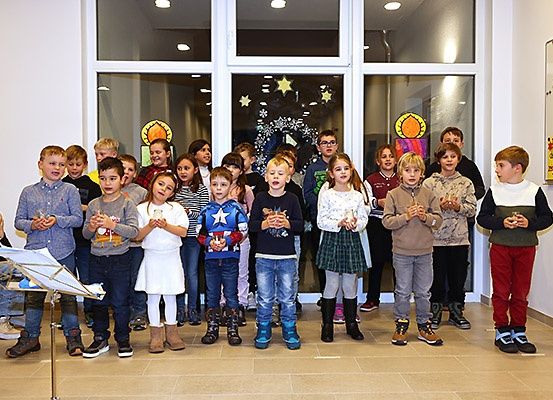 Eine Gruppe von Kindern und einigen Erwachsenen versammelt sich in einem Raum und singt. Die Kinder halten Kerzen.