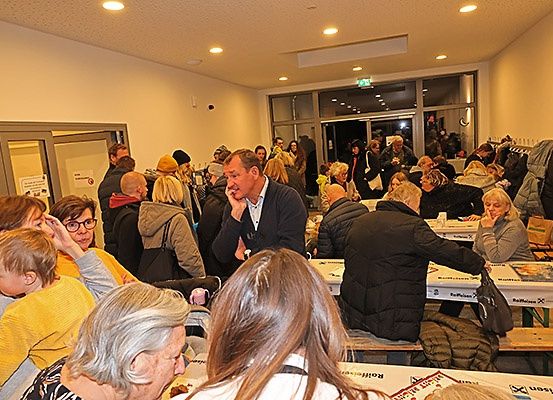Ein überfüllter Raum mit Menschen, die an Tischen sitzen, ein Mann telefoniert und andere unterhalten sich.