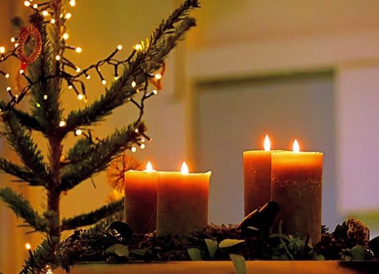 Ein kleiner Weihnachtsbaum mit brennenden Kerzen und Lichtern in einer Ecke.