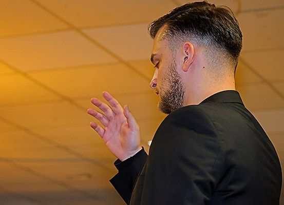 Ein Mann mit Bart betet mit geschlossenen Augen und erhobenen Händen in geschlossenen Räumen.