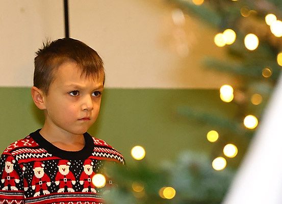 Ein junger Junge in einem Weihnachtspullover betrachtet einen geschmückten Weihnachtsbaum, umgeben von warmen gelben Lichtern.