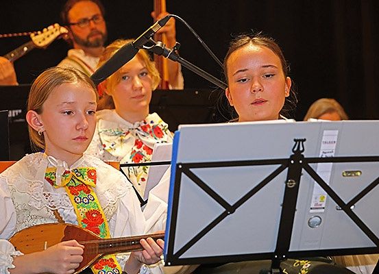 Drei Mädchen in traditioneller Kleidung spielen in einer Band Instrumente. Eine spielt eine Balalaika.