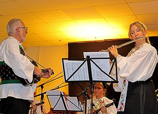 Ein älterer Mann spielt die Gitarre, während eine junge Frau die Flöte spielt. Sie werden von einem Geiger und einem Gitarristen begleitet.
