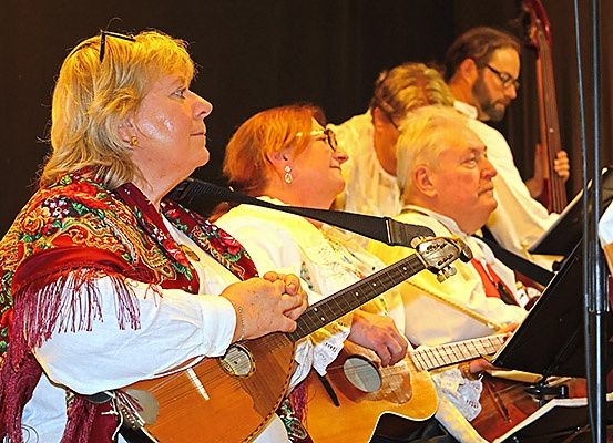 Eine Gruppe von Musikern, darunter eine Frau in einem weißen Hemd mit einem roten Schal, tritt mit Gitarren und anderen Instrumenten auf der Bühne auf.