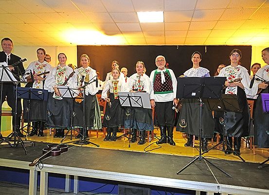 Eine Gruppe von Menschen steht auf der Bühne und spielt verschiedene Musikinstrumente wie Gitarren und Geigen. Sie sind in traditioneller Kleidung gekleidet.