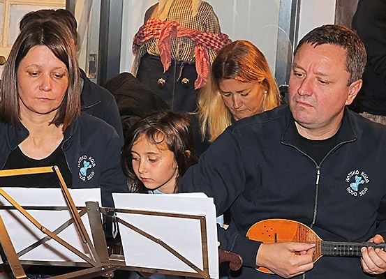 Eine Gruppe von Erwachsenen und Kindern schaut sich Notenblätter an. Der Mann spielt ein Musikinstrument.