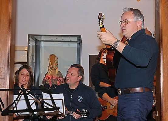 Eine Gruppe von Menschen spielt Gitarren in einem Raum mit einem hölzernen Pfeiler und einer Glasvitrine.