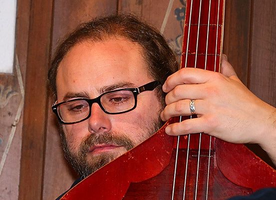 Ein Mann mit Brille und Bart spielt eine rote Kontrabass, während er nach unten schaut.