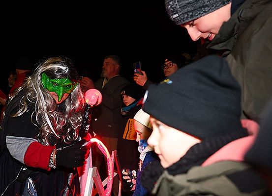 Eine Frau mit grüner Maske hält einen rosa Luftballon und ist von Leuten umgeben, die Fotos machen. Ein Kind hält einen leuchtenden rosa Luftballon.