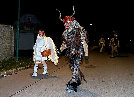 Eine Person in einem gehörnten Kostüm und eine andere in einem weißen Engelkostüm gehen nachts auf einer Straße.