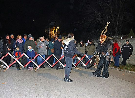 In der Nacht beobachtet eine Menschenmenge eine Person in einem gehörnten Kostüm, die einen Hockeyschläger hält. Sie sind von Barrikaden umgeben.