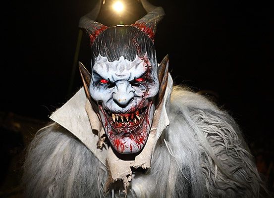 Eine Person in einem weißen pelzigen Kostüm mit einer Dämonenmaske mit roten Augen und Blut um den Mund.