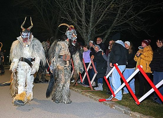Zwei Personen in Hörnermasken gehen bei Nacht eine Straße entlang, mit Zuschauern hinter Barrieren.