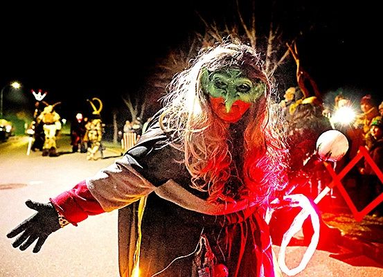 Eine Person in einem Kostüm mit grünem Gesicht und roten Highlights führt auf der Straße bei Nacht auf.