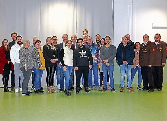 Eine Gruppe von Menschen, darunter Männer und Frauen, posiert für ein Foto in einem Raum. Sie stehen auf einem grünen Boden.