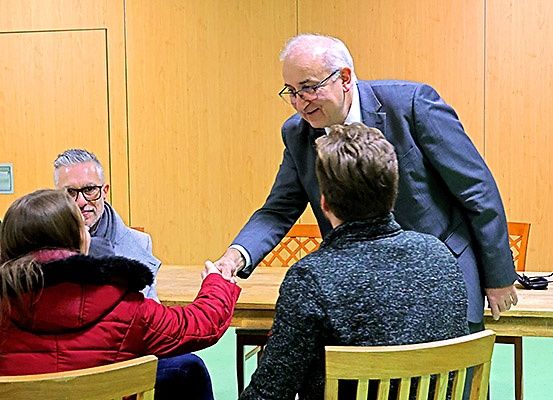Ein Mann in einem Anzug gibt zwei Personen in einem Raum mit Holzwänden die Hand.