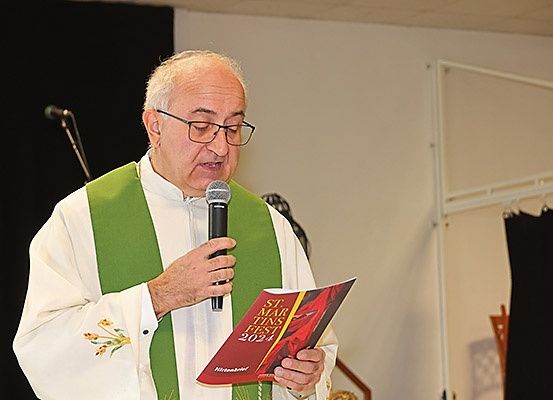 Ein Priester steht und hält ein Mikrofon und ein Buch mit dem Titel 'St. Martins Fest 2024', möglicherweise bei einer Veranstaltung.