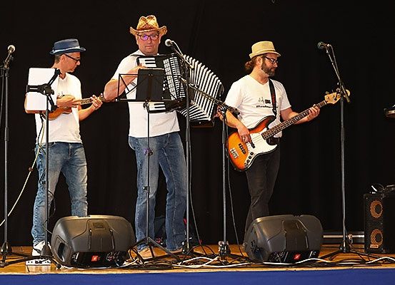 Drei Männer spielen auf der Bühne Gitarren und Akkordeon, mit Mikrofonen und Lautsprechern um sie herum.