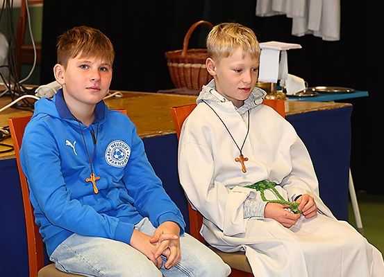 Zwei Jungen sitzen auf Stühlen. Einer trägt eine blaue Kapuzenjacke und der andere trägt eine weiße Robe. Sie schauen beide in eine Richtung.