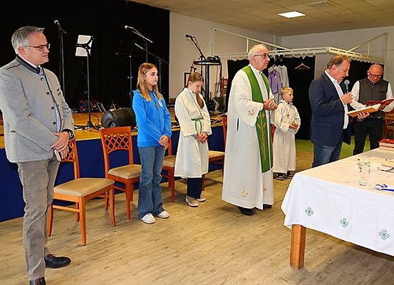 Ein Priester leitet eine Zeremonie mit einem Jungen und zwei Mädchen in weißen Gewändern vor ihm, während andere zuschauen.
