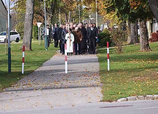 Eine Gruppe von Menschen in formeller Kleidung geht einen Weg in einer Außenumgebung, umgeben von Bäumen und Gras.