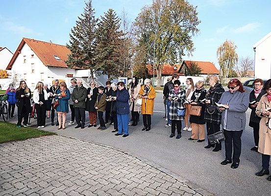 Eine Gruppe von Menschen steht in einer Reihe auf einer Straße, liest aus Büchern und hat Bäume und Gebäude im Hintergrund.