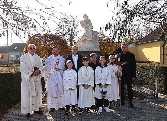 Eine Gruppe von Männern und Jungen in weißen Roben und Brillen steht vor einer Statue.