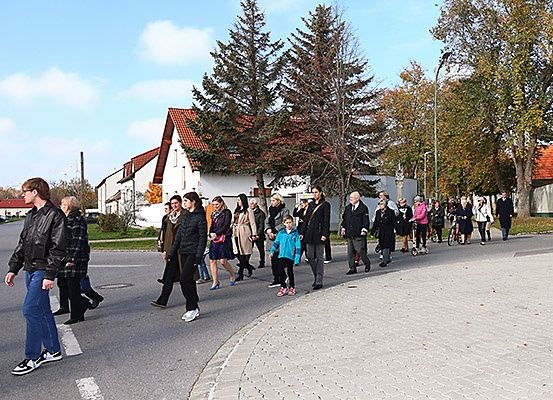 Eine Gruppe von Menschen, einschließlich Erwachsener und Kindern, geht in einer Kleinstadt über eine Straße. Einige tragen Jacken und Turnschuhe. Bäume und Häuser sind im Hintergrund.