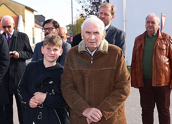 Eine Gruppe von Menschen steht auf einer Straße, darunter ein älterer Mann mit einem Stock, ein junger Junge und zwei ältere Männer in Lederjacken.
