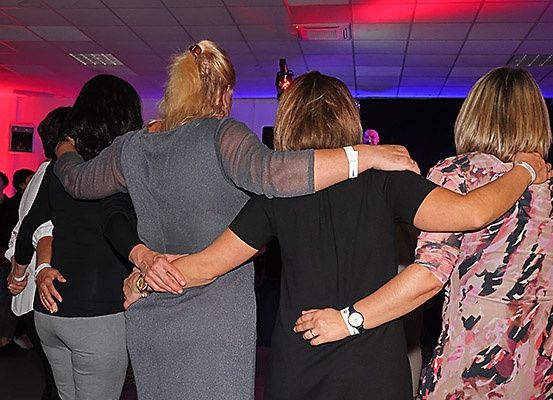 Eine Gruppe von Frauen tanzt in einem Raum mit roten und lila Lichtern zusammen.