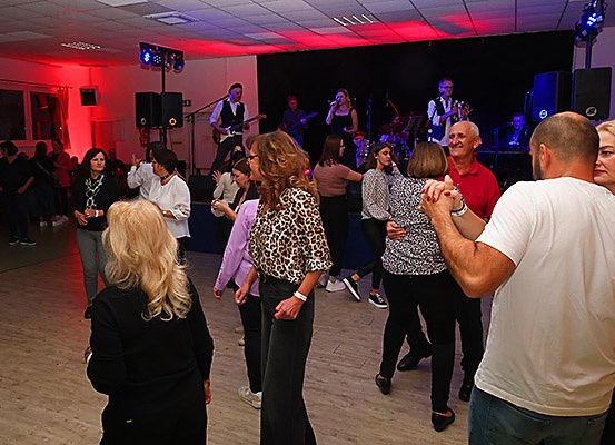 Eine Gruppe von Menschen tanzt in einem Raum mit roter Beleuchtung. Eine Band spielt auf der Bühne, und eine Frau singt.