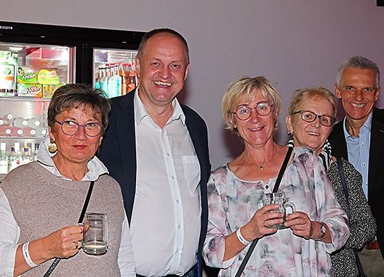 Fünf Personen, vier Frauen und ein Mann, posieren für ein Foto, während sie Gläser halten. Sie alle lächeln und stehen vor einem Kühlschrank.