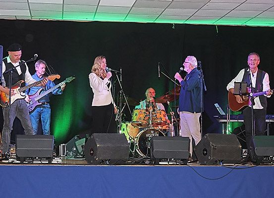 Eine Band spielt auf einer Bühne mit Mikrofonen, Gitarren und Trommeln unter grünen Scheinwerfern.