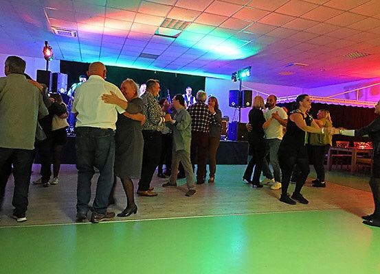Menschen tanzen bei einer Party mit Bühne, Lautsprechern und mehrfarbigen Lichtern, die den Raum erhellen.