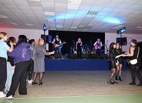 Eine Band spielt auf der Bühne mit Gitarren und Mikrofonen, während eine Gruppe von Menschen von unten zuschaut.