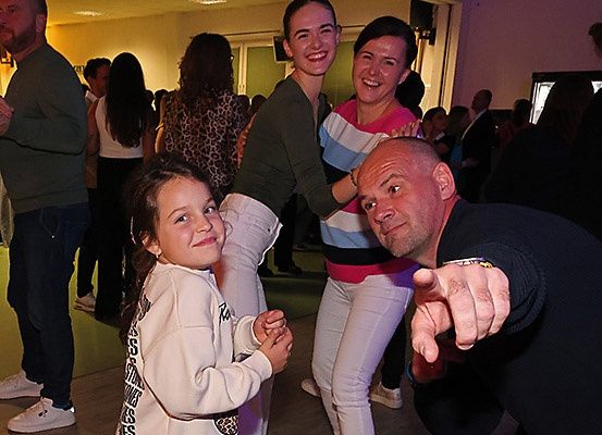 Mehrere Menschen tanzen in einem Raum. Ein Mädchen und ein Mann tanzen zusammen. Ein junges Mädchen lächelt. Eine ältere Frau tanzt mit einem Mädchen.