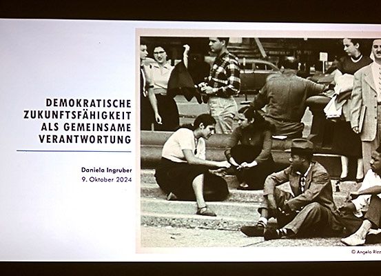Ein Schwarz-Weiß-Foto zeigt eine Gruppe von Menschen auf Stufen. Die Bildunterschrift lautet 'Demokratische Zukunftsfähigkeit als gemeinsame Verantwortung'. Das Datum unten ist der 9. Oktober 2024.