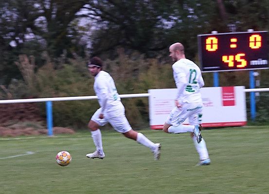 Zwei Fußballspieler verfolgen einen Ball auf einem Spielfeld, die Anzeigetafel zeigt 0:0 und 45 verbleibende Minuten.