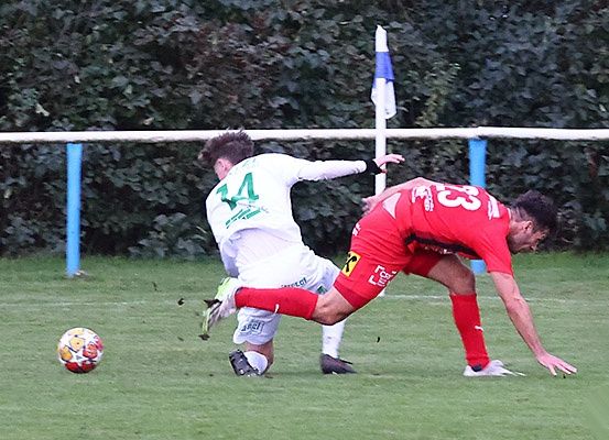 Zwei Fußballspieler in Aktion, einer in Rot und der andere in Weiß, konkurrieren auf einem Feld mit einem nahegelegenen Fußball.