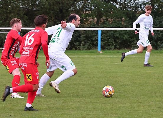 Fünf Fußballspieler in Trikots spielen auf einem Feld. Ein Spieler in Rot schaut einen in Weiß an. Sie jagen einem Ball nach.